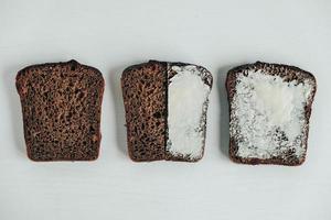 Sliced of brown bread with butter on a white wooden background. Top view. Copy, empty space for text photo