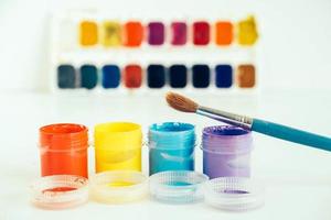 Colorful gouache paints and brush for painting on white wooden table photo