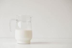 Glass jug with milk on a white table