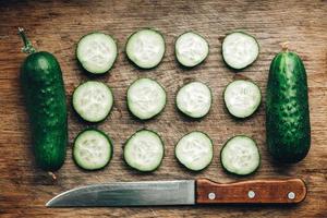Sliced fresh green cucumbers with a knife on a wooden background. Top view. Copy, empty space for text photo