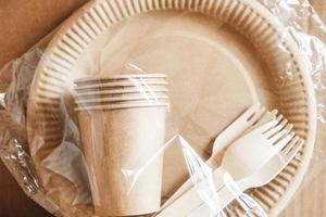 tenedores de madera y vasos de papel con platos sobre fondo de papel kraft. Vajilla desechable ecológica. también se utiliza en comida rápida, restaurantes, comida para llevar, picnics foto