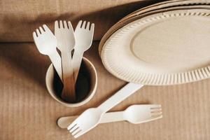 Wooden forks and paper cups with plates on kraft paper background. Eco friendly disposable tableware photo