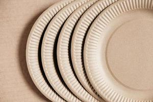 Disposable paper plates on kraft paper background. Eco friendly disposable tableware. Top view. Copy, empty space for text photo