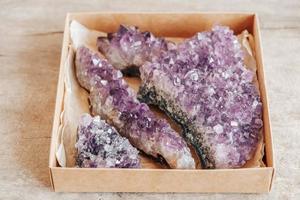 Violet amethyst crystals in a kraft paper box on wooden background photo