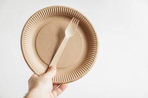 Men hand holding a wooden fork and disposable paper plate on white background