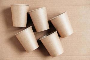 Disposable paper cups on kraft paper background. Eco friendly disposable tableware. Zero waste concept. Top view. Copy, empty space for text photo