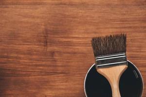 Open can of paint with brown brush on it on wooden background photo