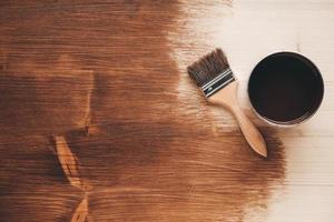 Open jar of brown paint with a brush on wooden background photo
