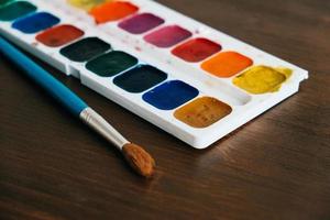 Set of watercolor paints with a brush for painting on a dark wooden background photo