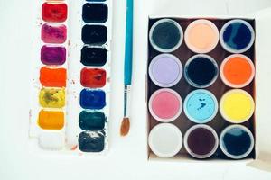 Colorful gouache paints and brushes for painting on white wooden table. Top view. Copy, empty space for text photo