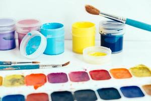 Colorful gouache paints and brushes for painting on white wooden table. Copy, empty space for text photo