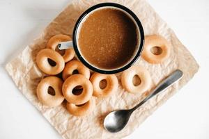 Metal mug with hot drink and mini round bagels on a white wooden background. Top view. Copy, empty space for text photo