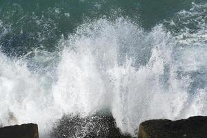 The waves breaking on a stony beach, forming a spray. Wave and splashes on beach. Waves crashing onto rocks. photo