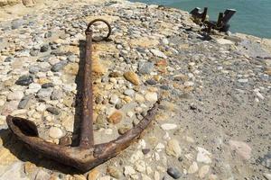 Old anchor lies on stones. Sunny day photo