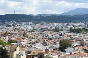 View of resort Greek architecture Rethymno city-port, built by Venetians, from height of Fortezza Castle - fortress on hill Paleokastro. Red tiled roofs and mountains in background. Crete. photo