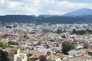 vista del complejo arquitectura griega ciudad-puerto de rethymno, construida por venecianos, desde la altura del castillo de fortezza - fortaleza en la colina paleokastro. techos de tejas rojas y montañas en el fondo. Creta. foto