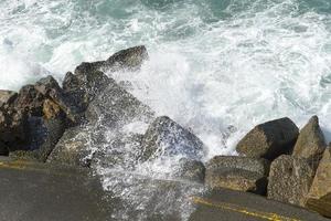 The waves breaking on a stony beach, forming a spray. Wave and splashes on beach. Waves crashing onto rocks. photo