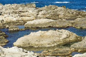 The waves breaking on a stony beach, forming a spray. Wave and splashes on beach. Waves crashing onto rocks. photo