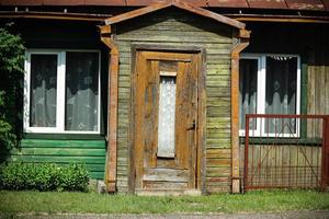 Old village wooden house front yard entrance with brown door and grass photo