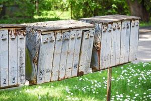Old gray rusty mail boxes in empty garden yard with green grass photo