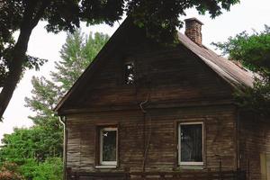 Old wooden house standing under a tree surrounded by greenery photo