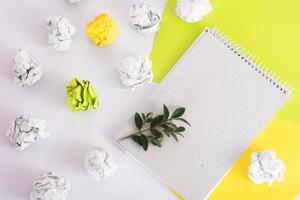 organic paper notebook with green twig among crumpled paper and colored paper on white background. zero waste concept
