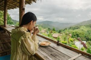 Asian woman drinking hot cocoa, toast on balcony among the mountain photo