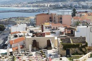 vista del complejo arquitectura griega ciudad-puerto de rethymno, construida por venecianos, desde la altura del castillo de fortezza - fortaleza en la colina paleokastro. techos de tejas rojas y montañas en el fondo. Creta. foto