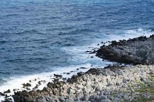 The waves breaking on a stony beach, forming a spray. Wave and splashes on beach. Waves crashing onto rocks. photo