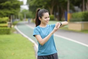 mujer joven feliz en ropa deportiva usando reloj inteligente mientras hace ejercicio en el parque foto