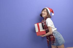 Portrait of beautiful woman wearing red Santa Claus hat holding gift box over studio background, Christmas and New Year Concept photo