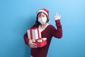 Portrait of young smiling woman in surgical mask wearing red Santa Claus hat isolated blue background studio. photo