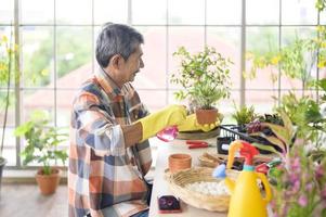 Happy senior asian retired man spraying and watering tree  enjoys  leisure activity at home photo