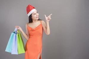 Portrait of young smiling woman wearing red Santa Claus hat is holding credit card and colorful shopping bag isolated gray background studio, Christmas and New Year Concept. photo