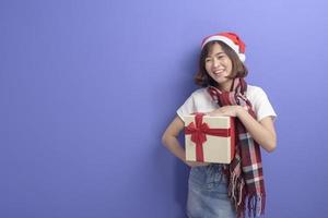 Portrait of beautiful woman wearing red Santa Claus hat holding gift box over studio background, Christmas and New Year Concept photo