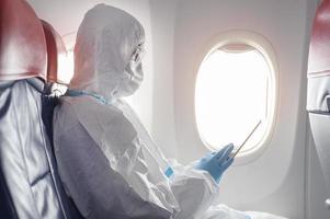 An Asian man is wearing protective suit , PPE suit in airplane , safety travel concept . photo