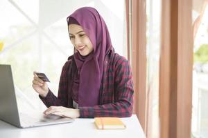 mujer musulmana con hiyab está trabajando con una computadora portátil en una cafetería foto