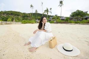 una hermosa mujer feliz con vestido blanco disfrutando y relajándose en el concepto de playa, verano y vacaciones foto