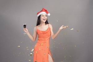Portrait of beautiful woman wearing red Santa Claus hat celebrating and playing paper shoot isolated gray background studio, Christmas and New Year Concept. photo