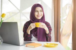 Muslim woman with hijab is working with laptop computer in coffee shop photo