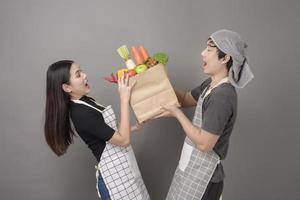 Happy couple is holding vegetables in grocery bag in studio grey  background photo