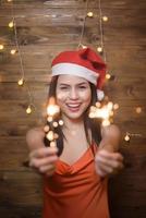 retrato de mujer hermosa con santa claus rojo sosteniendo bengalas en casa, concepto de navidad y año nuevo. foto