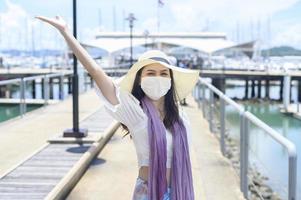 A traveller woman is wearing protective mask in on the dock, travel under Covid-19 pandemic, safety travels, social distancing protocol, New normal travel concept photo