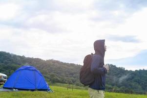 Happy traveling man enjoying and relaxing near camp tent over beautiful green mountain in rainy season, Tropical climate. photo