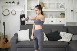 Beautiful young woman in sportswear exercising with dumpbells at home photo