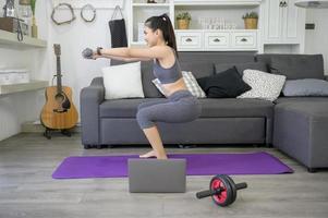 Beautiful young woman in sportswear exercising with dumpbells at home photo