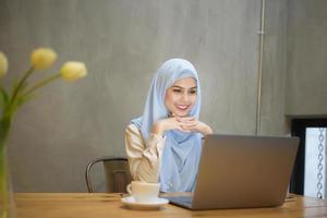 mujer musulmana con hiyab está trabajando con una computadora portátil en una cafetería foto