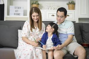 Happy asian parent teaching little cute daughter to do homework and drawing picture together at home. photo