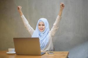 mujer musulmana con hiyab está trabajando con una computadora portátil en una cafetería foto