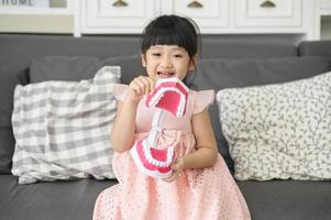 una niña linda sostiene un modelo dental artificial de mandíbula humana en el interior, educación y concepto de salud. foto